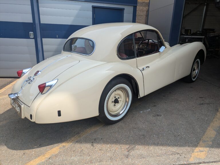 Cream classic Jaguar XK coupe parked outside a specialist classic vehicle restoration workshop.