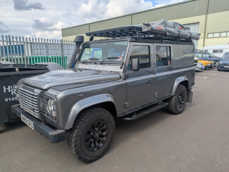 Grey Land Rover Defender 110 with roof rack and off-road accessories outside Trickett Welding.